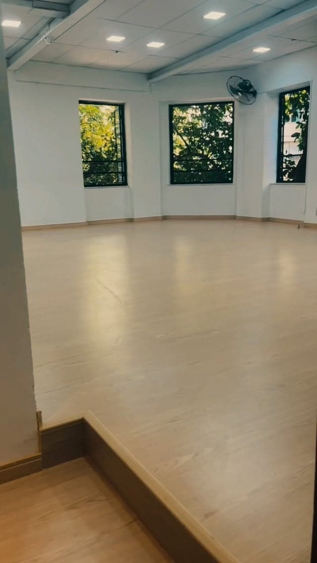Sala de dança vazia da NOXI, com piso de madeira e janelas para o verde, em Copacabana